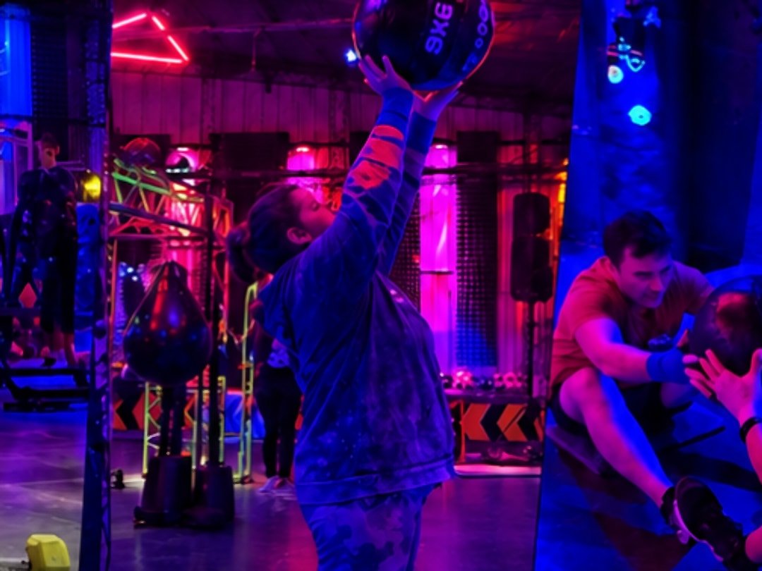 Alumna levantando una pelota medicinal en la sala iluminada con neón